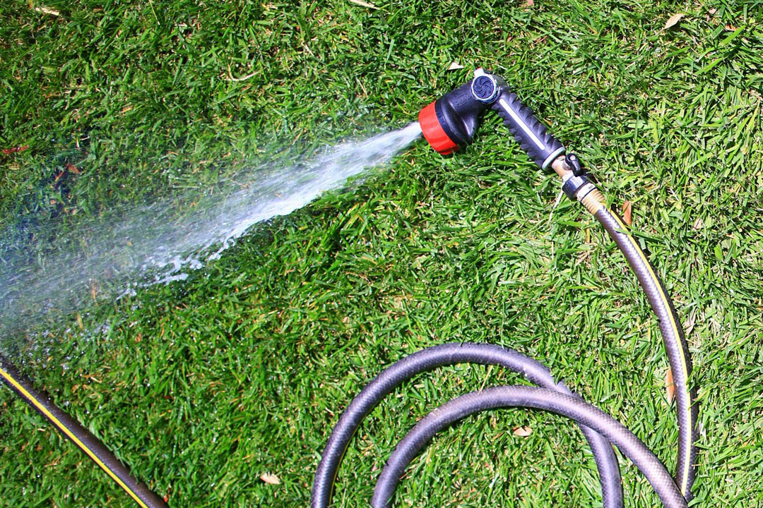 Person watering indoor houseplants using a lightweight coil hose with a spray wand attached to a sink faucet